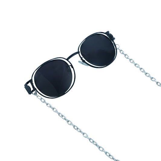 A pair of round, dark-lensed sunglasses with a silver frame is connected to a silver chain, which holds a pendant shaped holographic vibrant rainbow crystal-frame view