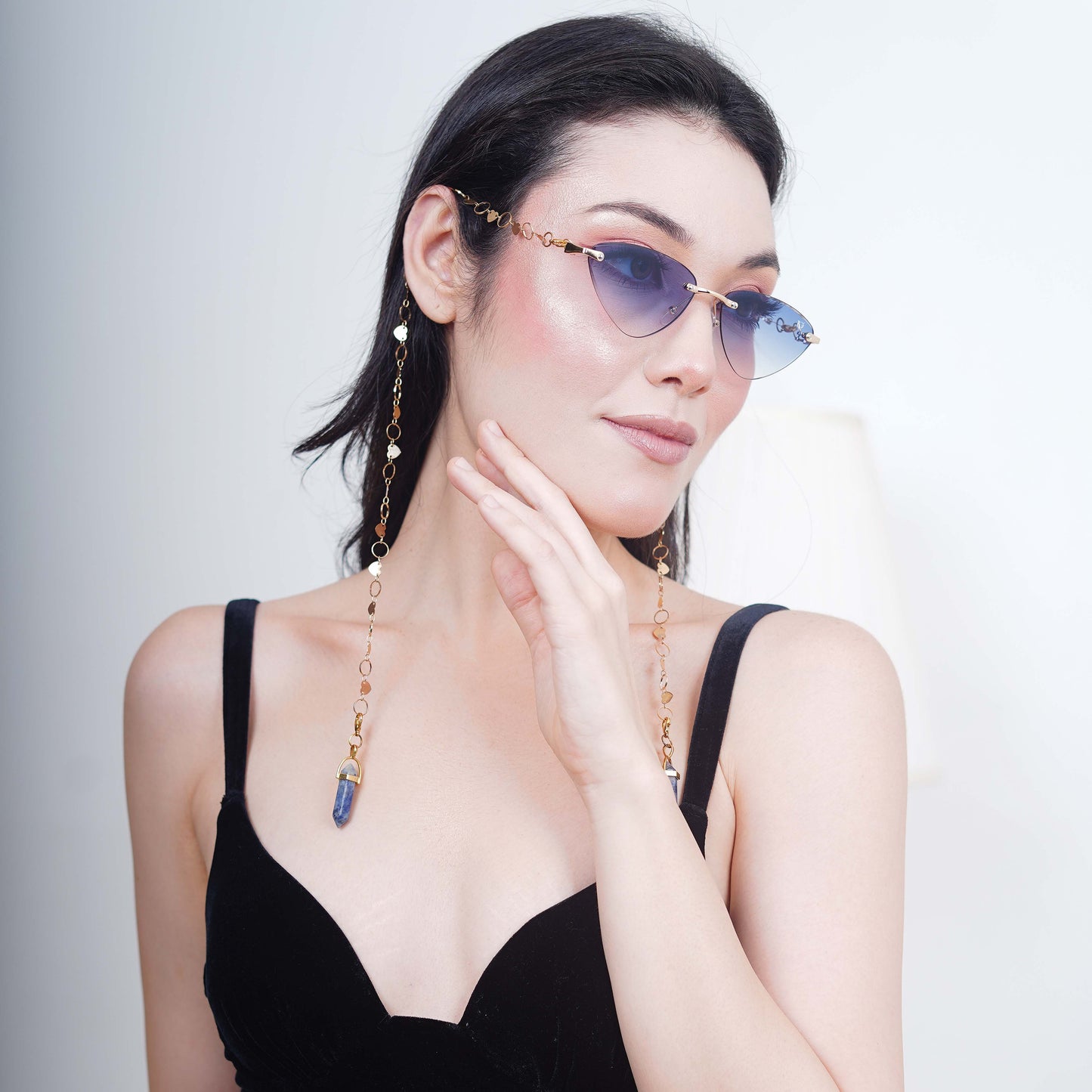 Authentic cat-eye frames with blue gradient-tinted lenses adorned with a gold-toned dual-linker chain of oval rings and leaf discs with vibrant blue charms-right angle pose