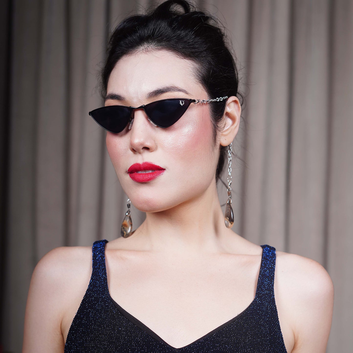 Bold, pointed black cat eye frames attached with a gold chain and adorned with gold-brown gradient clear charms-side view