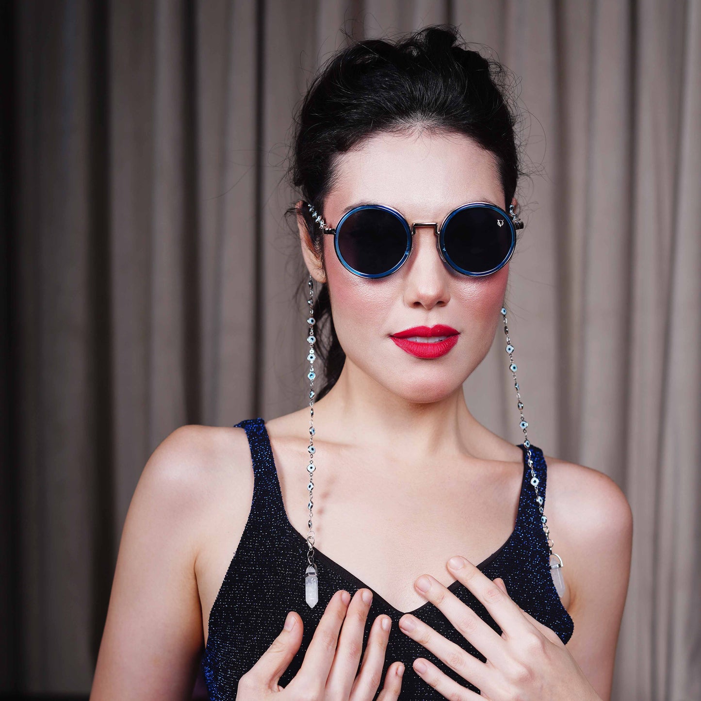 Trendy oversized blue round lenses adorned with a silver-tone evil eye chain and translucent white charm for a fashion statement-styling pose