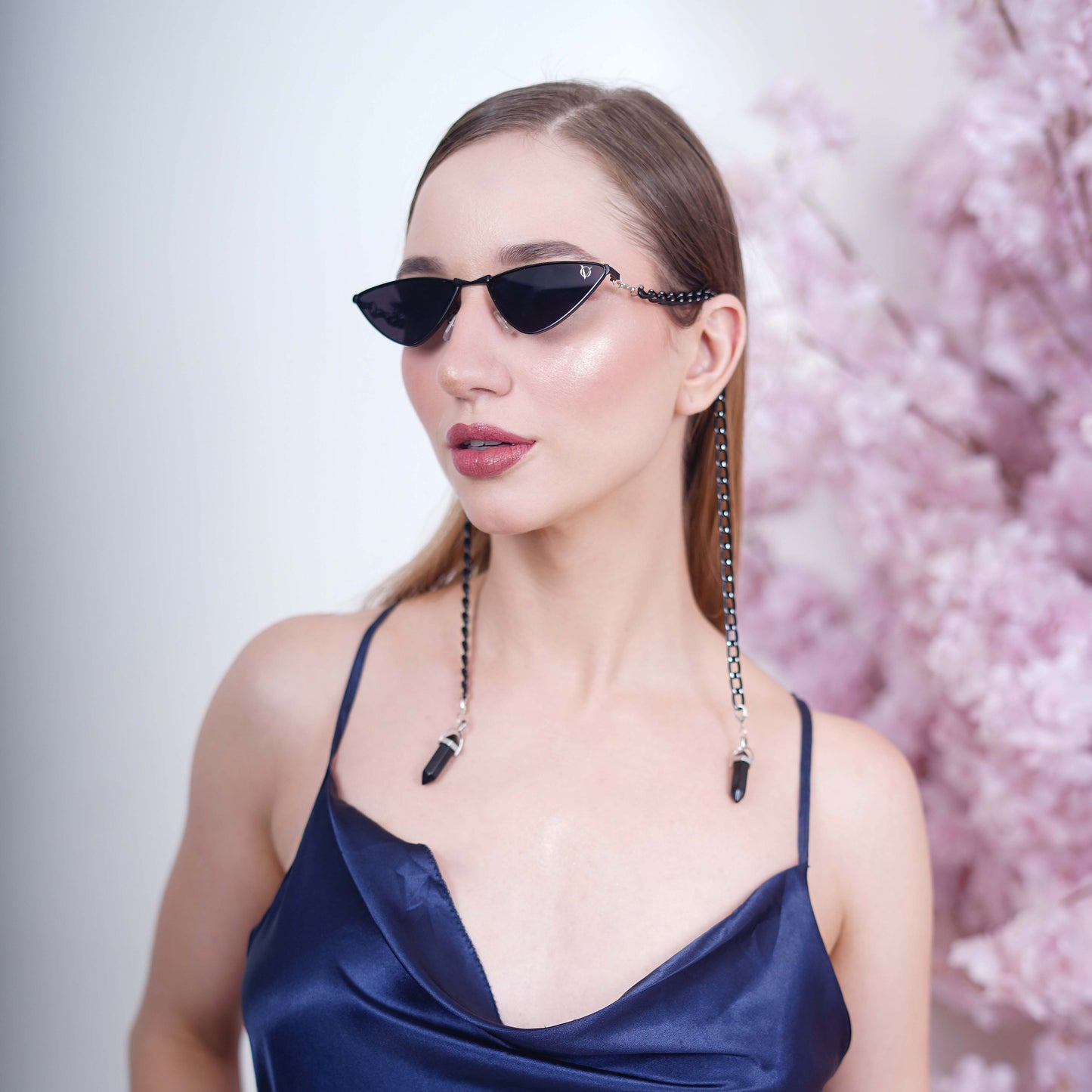 Vibrant cat-eye framed dark sunglasses with a black metal chain attached with a black charm with a silver finished metal holder-angle view