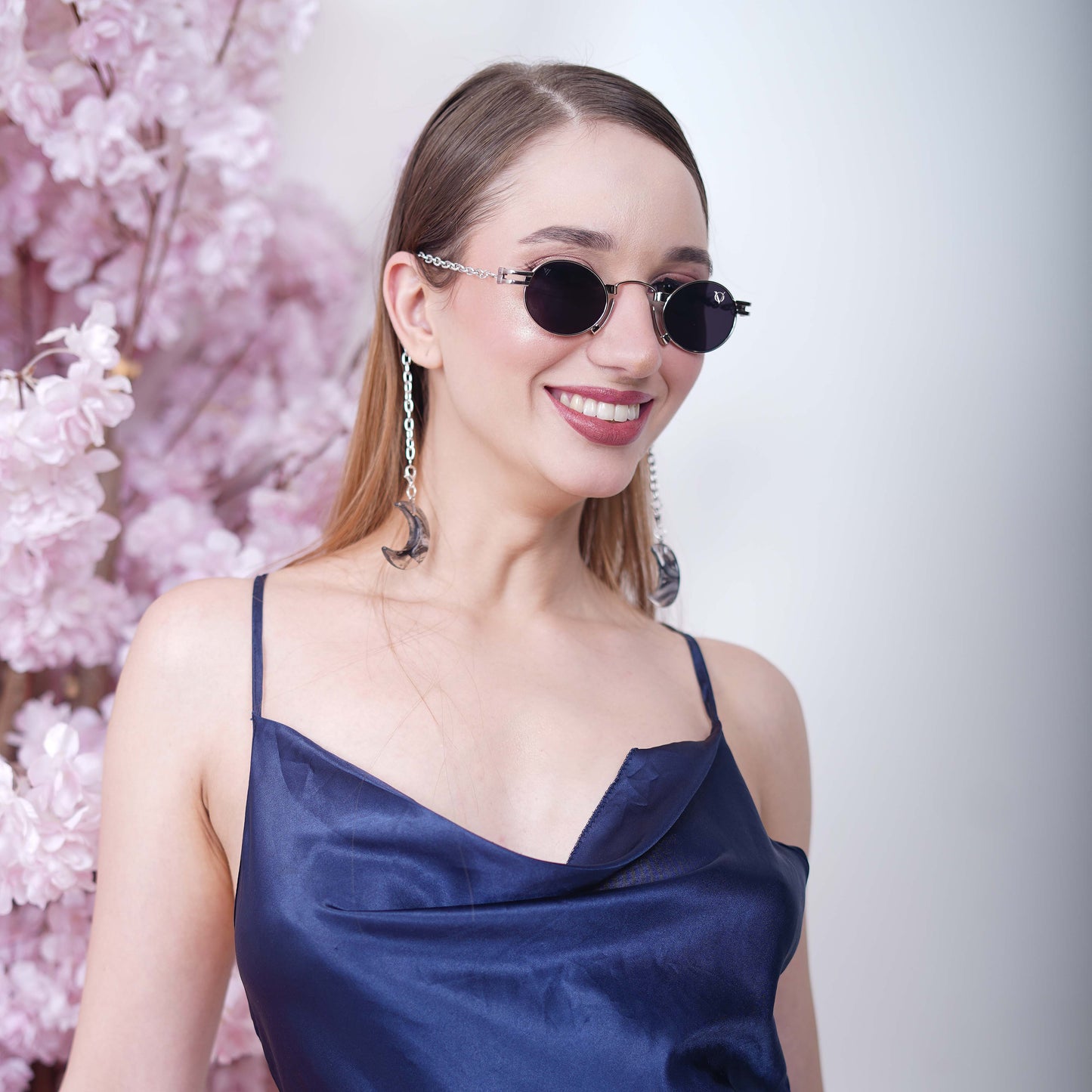 Charming oval-shaped frames with blue-tinted silver finished lenses attached with a silver chain and adorned with crescent-shaped bluish-green gradient charms-smiling view