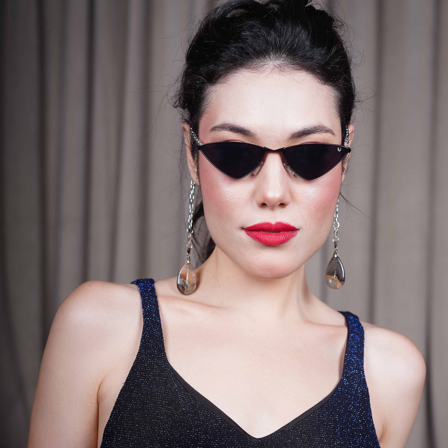 Bold, pointed black cat eye frames attached with a gold chain and adorned with gold-brown gradient clear charms-front view