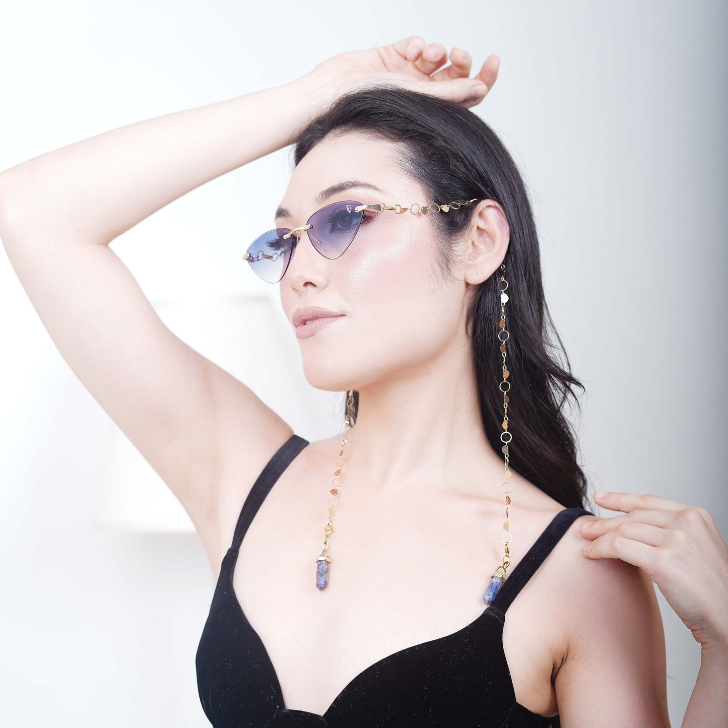 Authentic cat-eye frames with blue gradient-tinted lenses adorned with a gold-toned dual-linker chain of oval rings and leaf discs with vibrant blue charms-angle pose