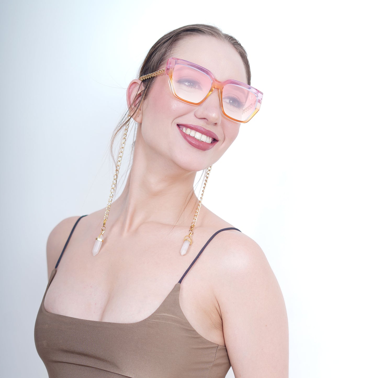 Trendy oversized orange-pink gradient large orange colored sunglasses with a golden chain and translucent white charms-side smiling view