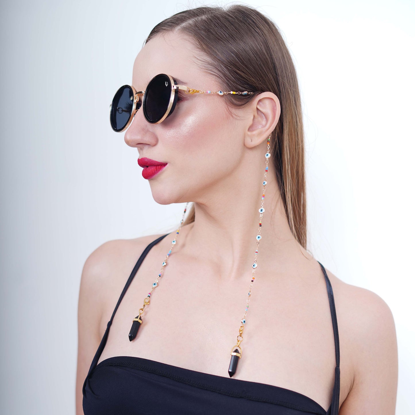 Large round sunglasses with dark shade golden finishing lenses adorned with evil-eye multi-colored gold chain and black charms with gold metal holder-side pose