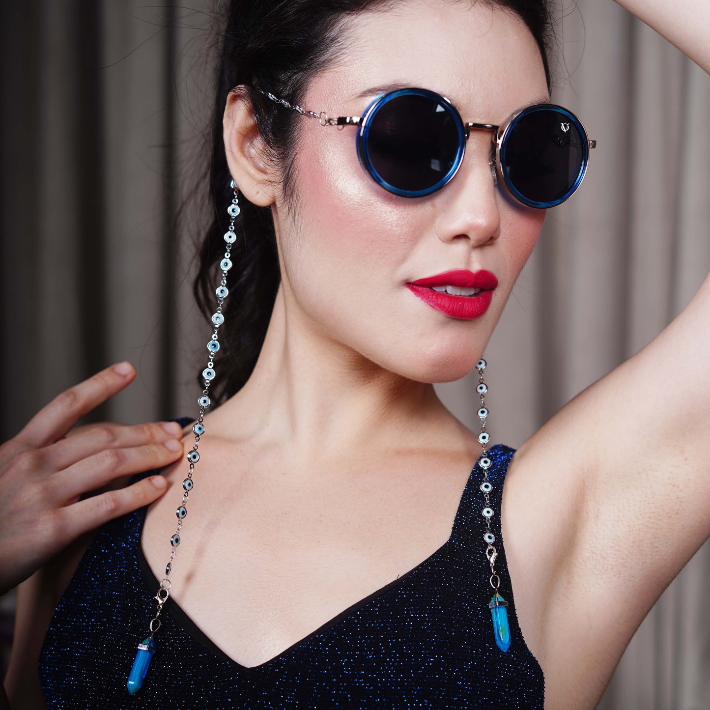 Round black lenses with gold frame attached to evil-eye beaded silver chain attached to blue stone charm with a silver cap-angle view