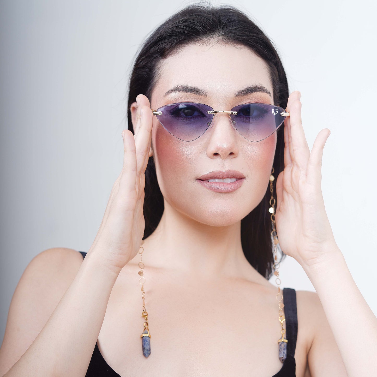 Authentic cat-eye frames with blue gradient-tinted lenses adorned with a gold-toned dual-linker chain of oval rings and leaf discs with vibrant blue charms-styling pose