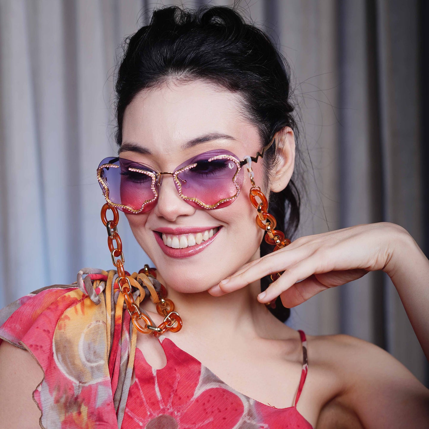 Shimmery red-purple gradient lens with gold glittery boundary attached with orange oval rings chain with gold linker-angle view