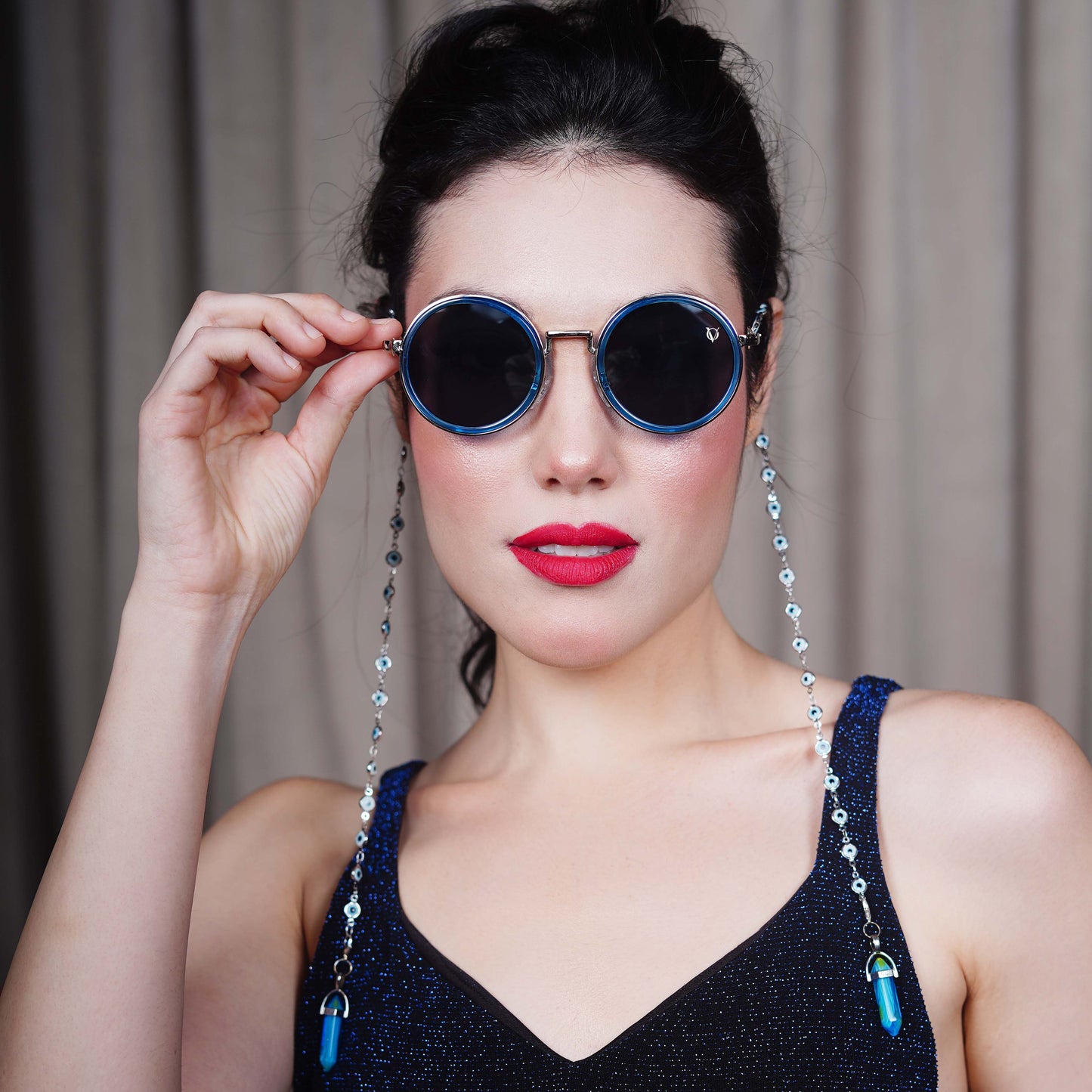 Round black lenses with gold frame attached to evil-eye beaded silver chain attached to blue stone charm with a silver cap-model view