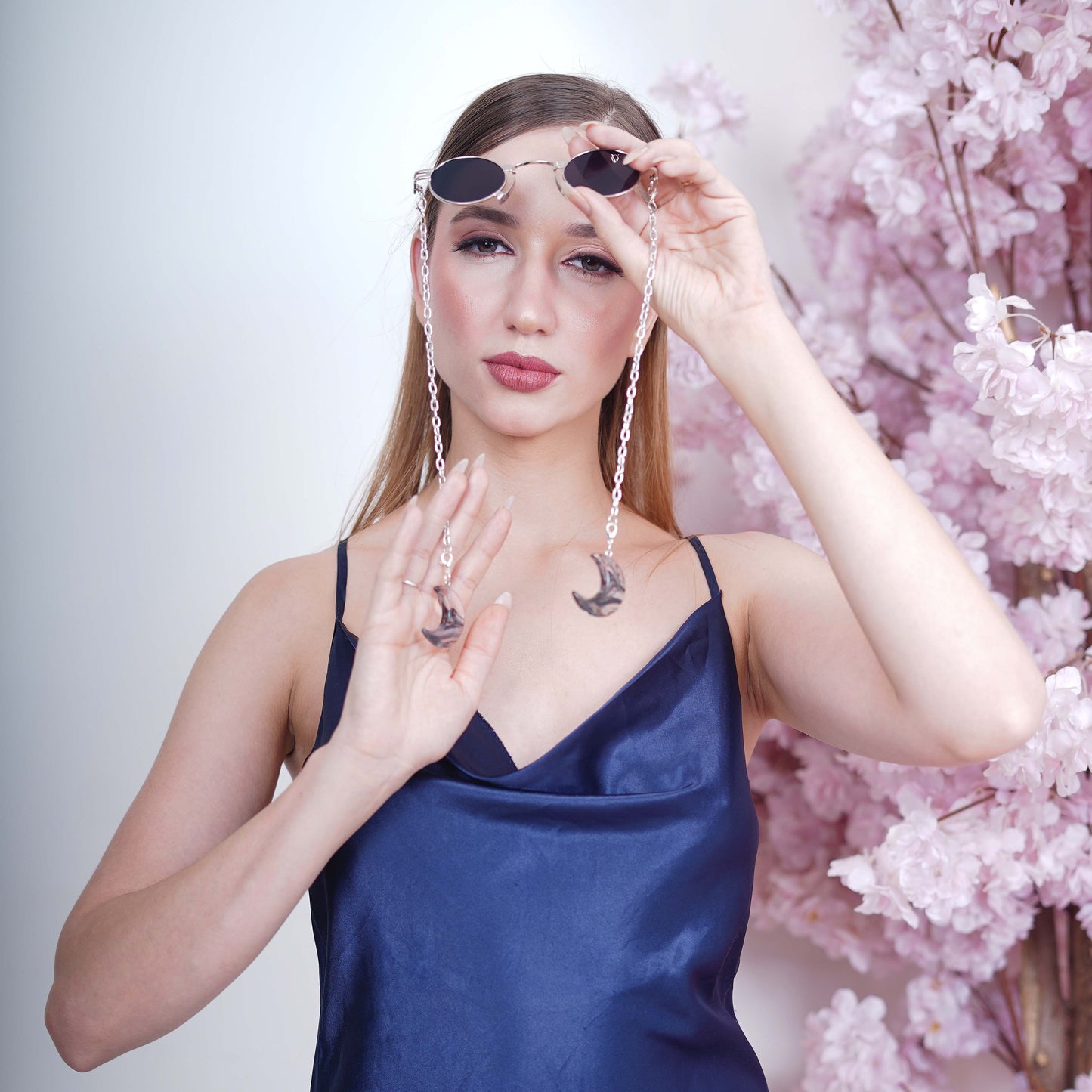 Charming oval-shaped frames with blue-tinted silver finished lenses attached with a silver chain and adorned with crescent-shaped bluish-green gradient charms-angle view