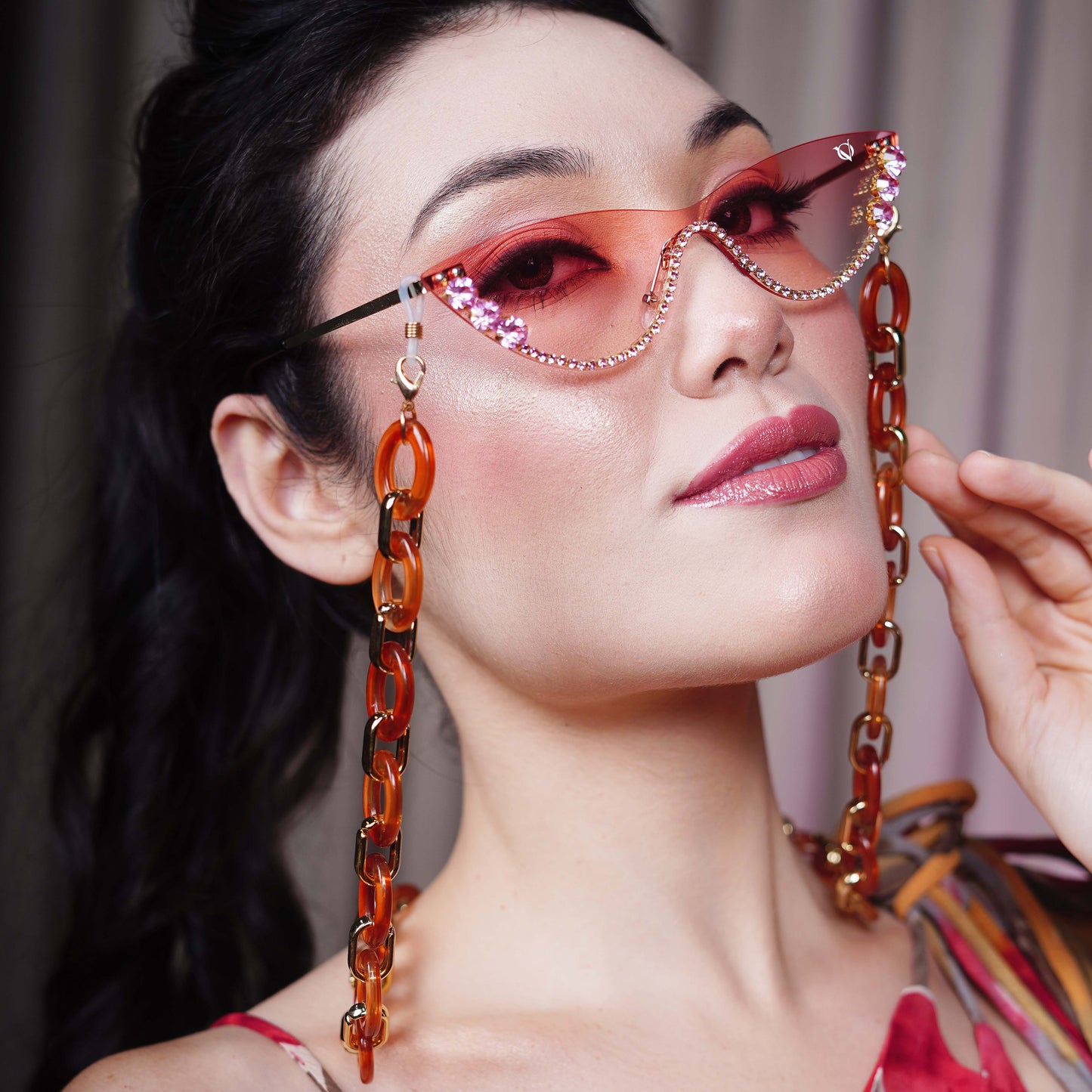 stylish pink sunglasses with gemstone frame and long orange chain attachments-side view