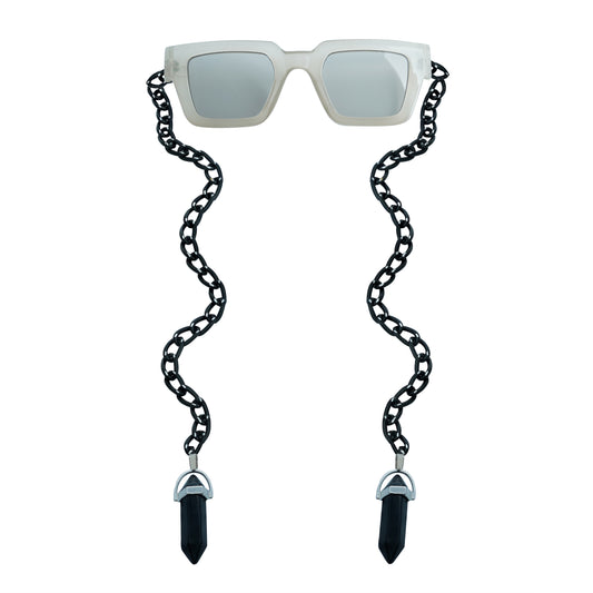 Oversized sqaure framed sunglasses with a white bold frame is connected to a black chain, which holds a pendant shaped black crystal-front view