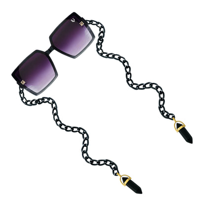 Square sunglasses with dark purple gradient lenses attached to a black chain featuring gold detailing-angle view