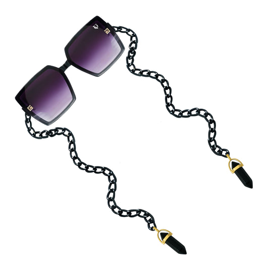 Square sunglasses with dark purple gradient lenses attached to a black chain featuring gold detailing-angle view
