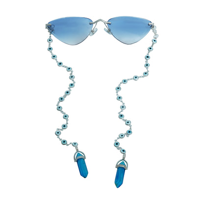 A pair of cat-eye framed sunglasses with a silver frame is connected to a silver evil-eye chain, which holds a pendant shaped blue crystal(Blue Stone)-whole view