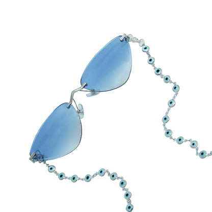 A pair of cat-eye framed sunglasses with a silver frame is connected to a silver evil-eye chain, which holds a pendant shaped blue crystal(Blue Stone)-frame view