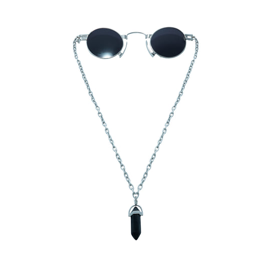 Round oval shaped sunglasses with a silver metallic frame attached to black chain, which holds a pendant shaped black crystal-front view