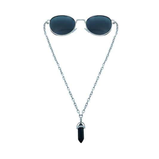 A pair of round, dark-lensed sunglasses with a silver frame is connected to a silver chain, which holds a pendant shaped black crystal-front view