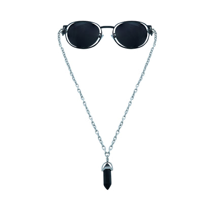 Round oval shaped sunglasses with a silver metallic frame attached to silver chain, which holds a pendant shaped black crystal-front view
