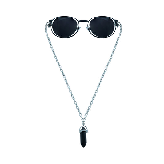 Round oval shaped sunglasses with a silver metallic frame attached to silver chain, which holds a pendant shaped black crystal-front view