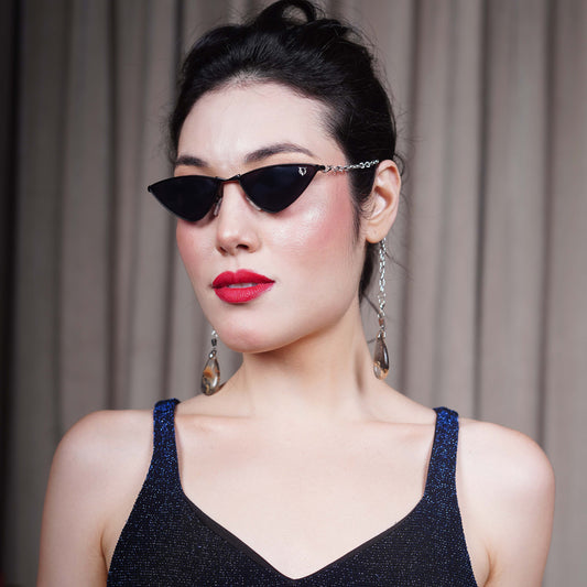 Bold, pointed black cat eye frames attached with a gold chain and adorned with gold-brown gradient clear charms-side view