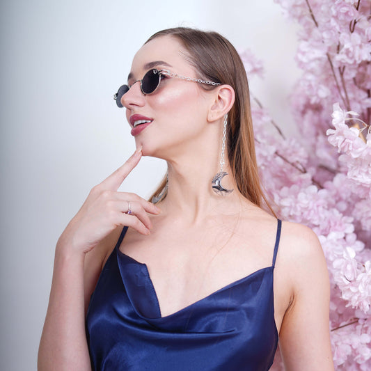 Charming oval-shaped frames with blue-tinted silver finished lenses attached with a silver chain and adorned with crescent-shaped bluish-green gradient charms-angle view