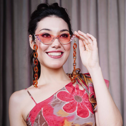 stylish pink sunglasses with gemstone frame and long orange chain attachments-front view
