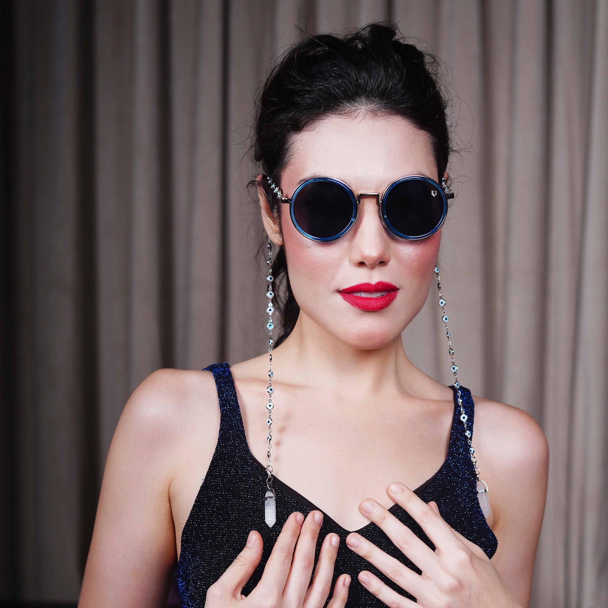 Trendy oversized blue round lenses adorned with a silver-tone evil eye chain and translucent white charm for a fashion statement-styling pose   

