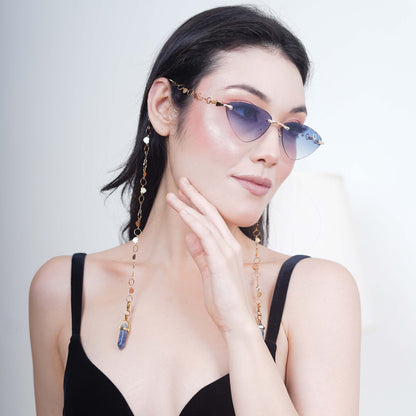 Authentic cat-eye frames with blue gradient-tinted lenses adorned with a gold-toned dual-linker chain of oval rings and leaf discs with vibrant blue charms-side angle pose