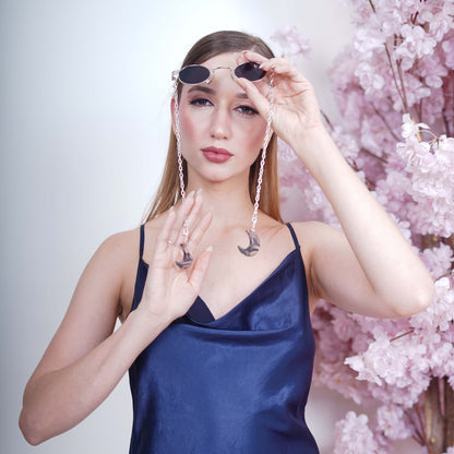 Charming oval-shaped frames with blue-tinted silver finished lenses attached with a silver chain and adorned with crescent-shaped bluish-green gradient charms-angle view