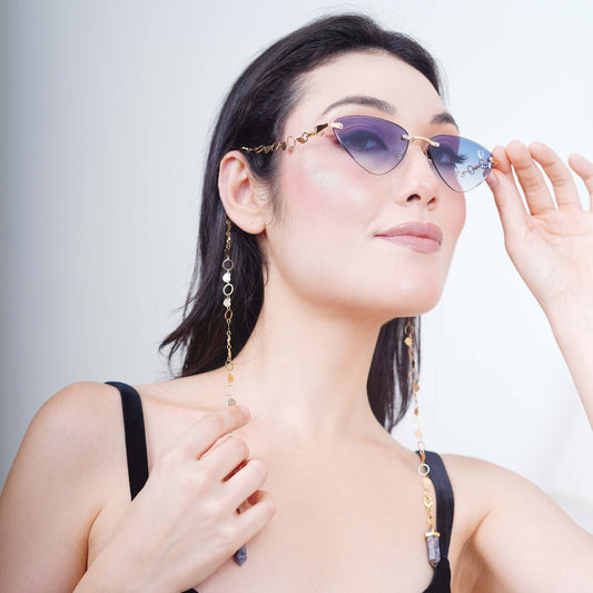 Authentic cat-eye frames with blue gradient-tinted lenses adorned with a gold-toned dual-linker chain of oval rings and leaf discs with vibrant blue charms-side pose