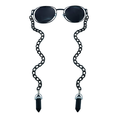 A pair of round, dark-lensed sunglasses with a silver frame is connected to a black chain, which holds a pendant shaped black crystal(Obsidian Stone)-front view