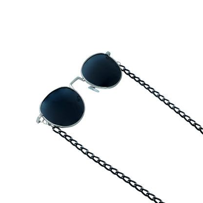 A pair of round, dark-lensed sunglasses with a silver frame is connected to a black chain, which holds a pendant shaped holographic vibrant rainbow crystal-frame view