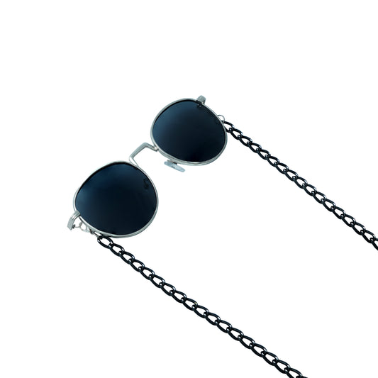 A pair of round, dark-lensed sunglasses with a silver frame is connected to a black chain, which holds a pendant shaped holographic vibrant rainbow crystal-frame view
